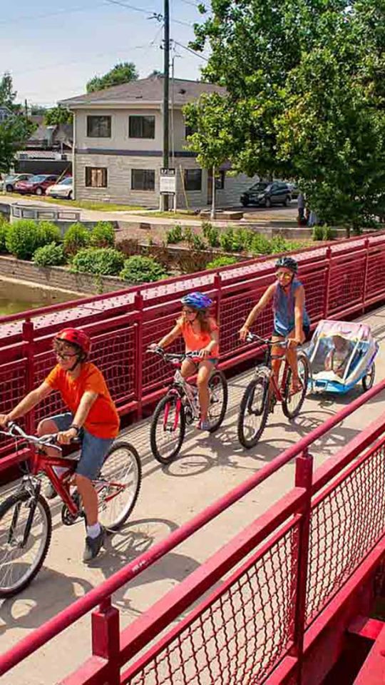 people riding bikes on a red bridge over a river at The Edgewater