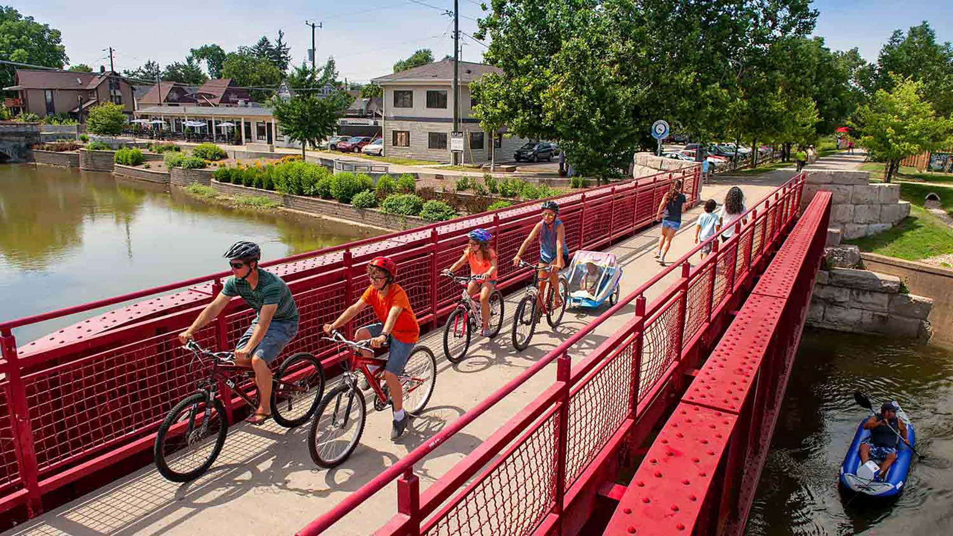 people riding bikes on a red bridge over a river at The Edgewater